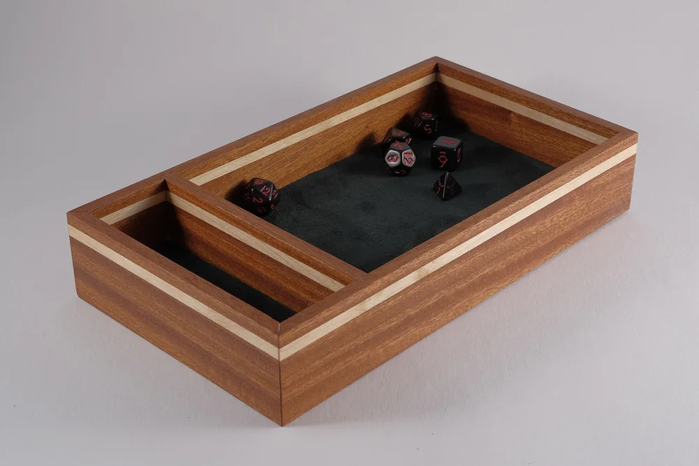A canarywood dice tray with maple accents and a black faux suede floor, with dice inside