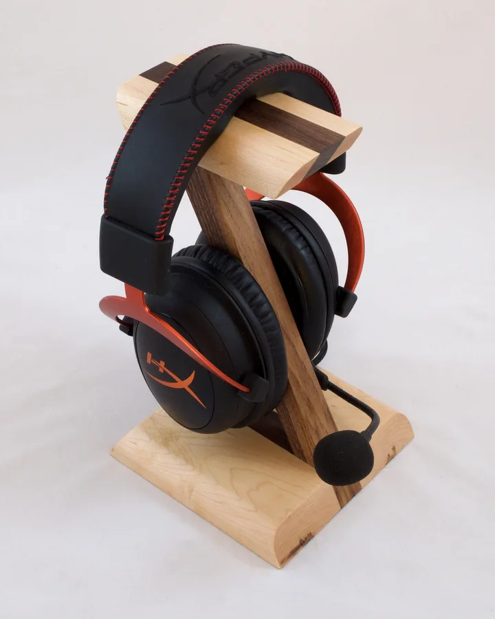 A Z-shaped headphone stand in maple and walnut holding a pair of black and red headphones